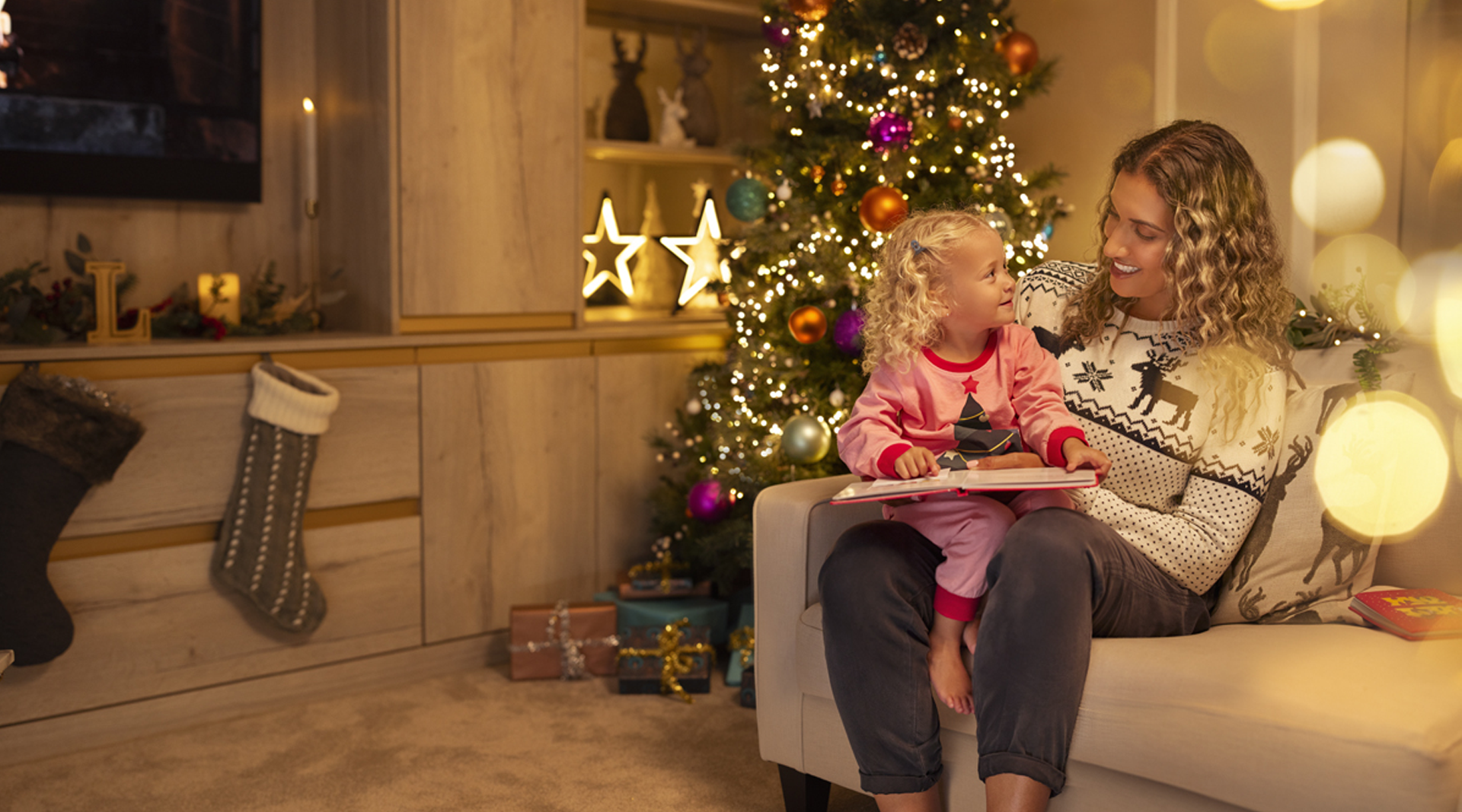 a mother and daughter sat on a sofa reading a scrapbook, with Christmas decorations adorning the room.